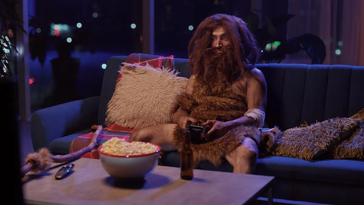 A cave man playing video games late at night instead of sleeping, showing the absurdity of our lifestyle